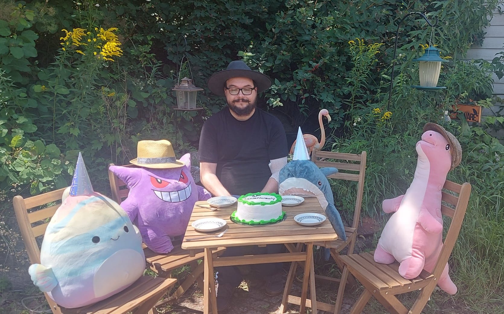 A man with facial hair and a felt sun hat has joined stuffed animal patio party, Photo 1